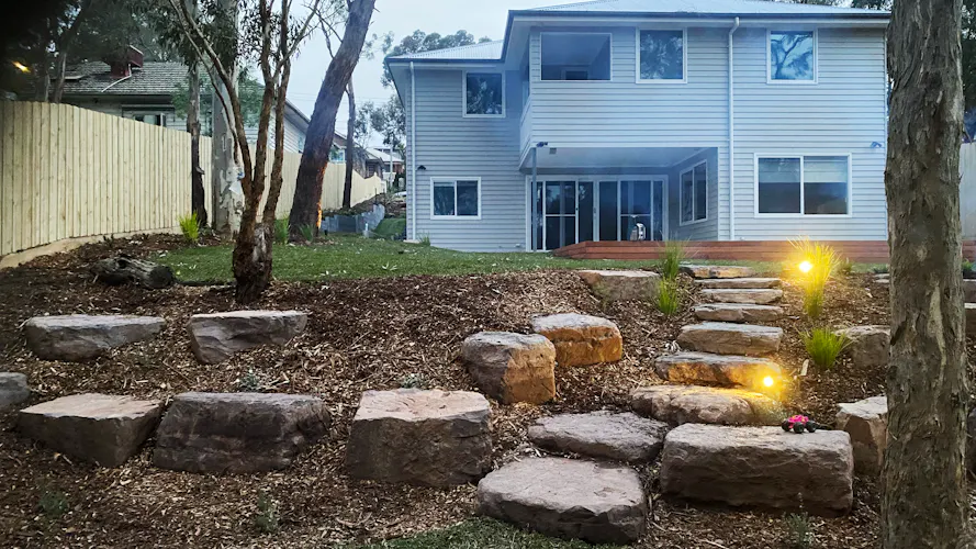 Family home in Montmorency, Melbourne with full front and backyard landscaping by Land Sculpture shown at dusk with garden lighting
