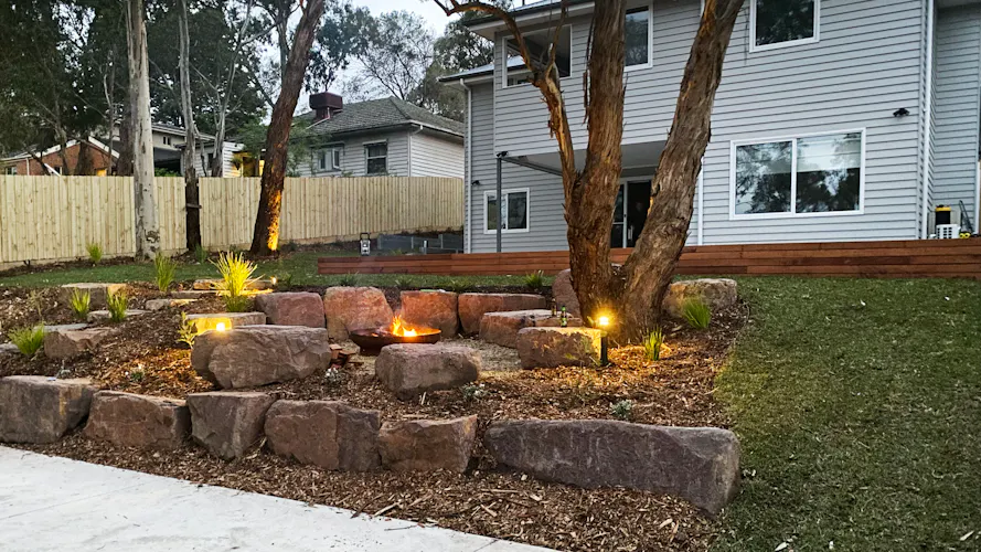 Family home in Montmorency, Melbourne with full front and backyard landscaping by Land Sculpture shown at dusk with garden lighting and fire pit
